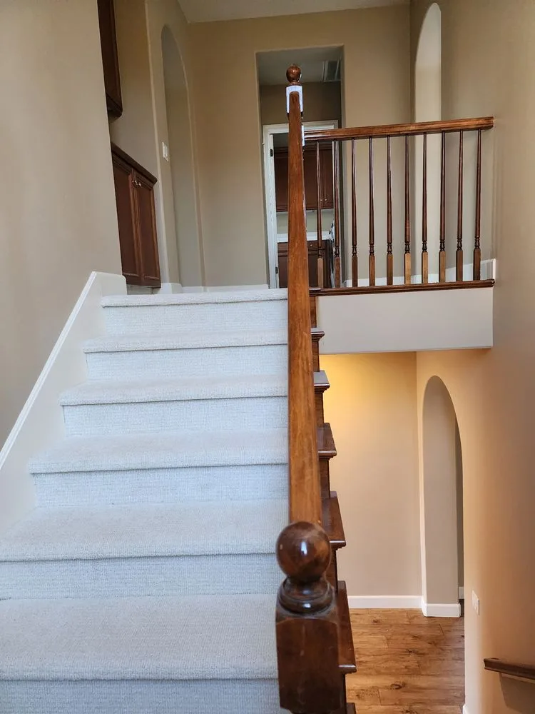 Light carpet installed on a residential staircase with wood railing by The Flooring Design Center