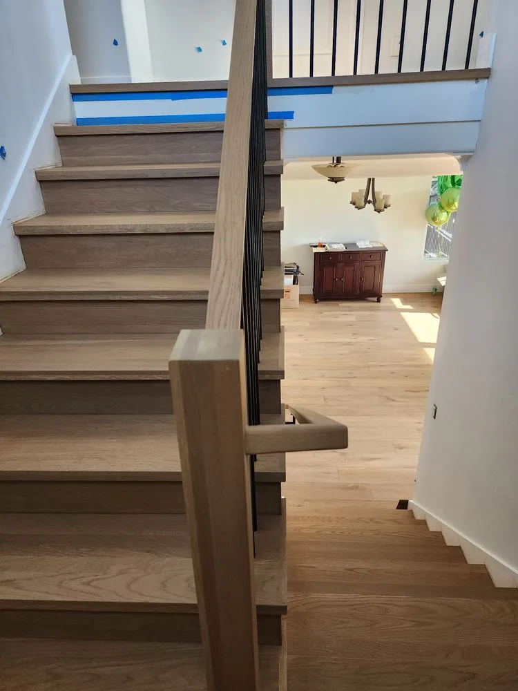 Light wood staircase and flooring with black metal railing installed by The Flooring Design Center